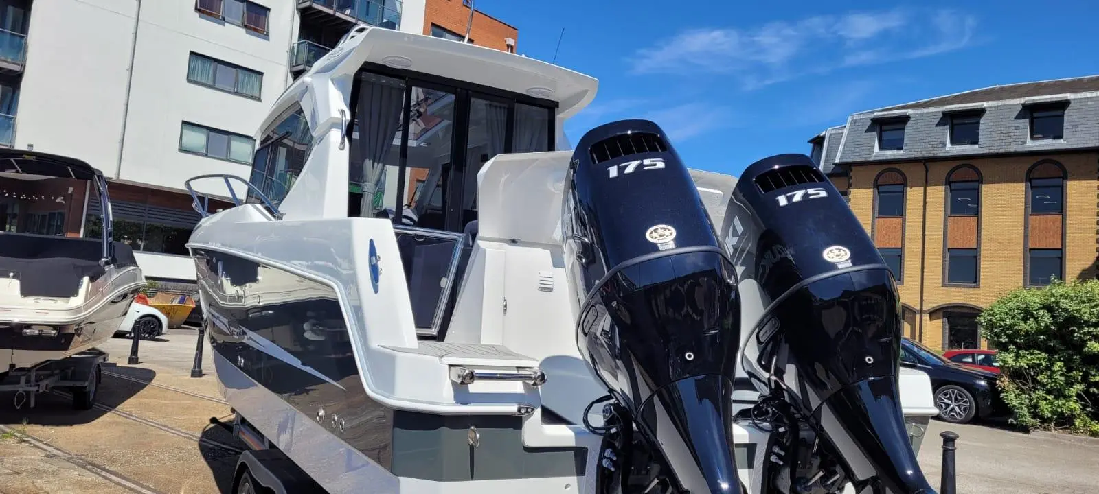 A sleek motorboat with twin 175 HP engines parked near buildings, showcasing modern design and marina lifestyle.